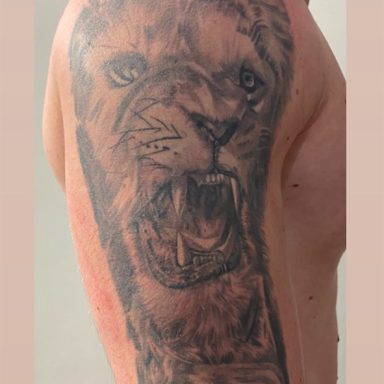 Tattoo van een aanvaltende leeuw op de bovenarm.